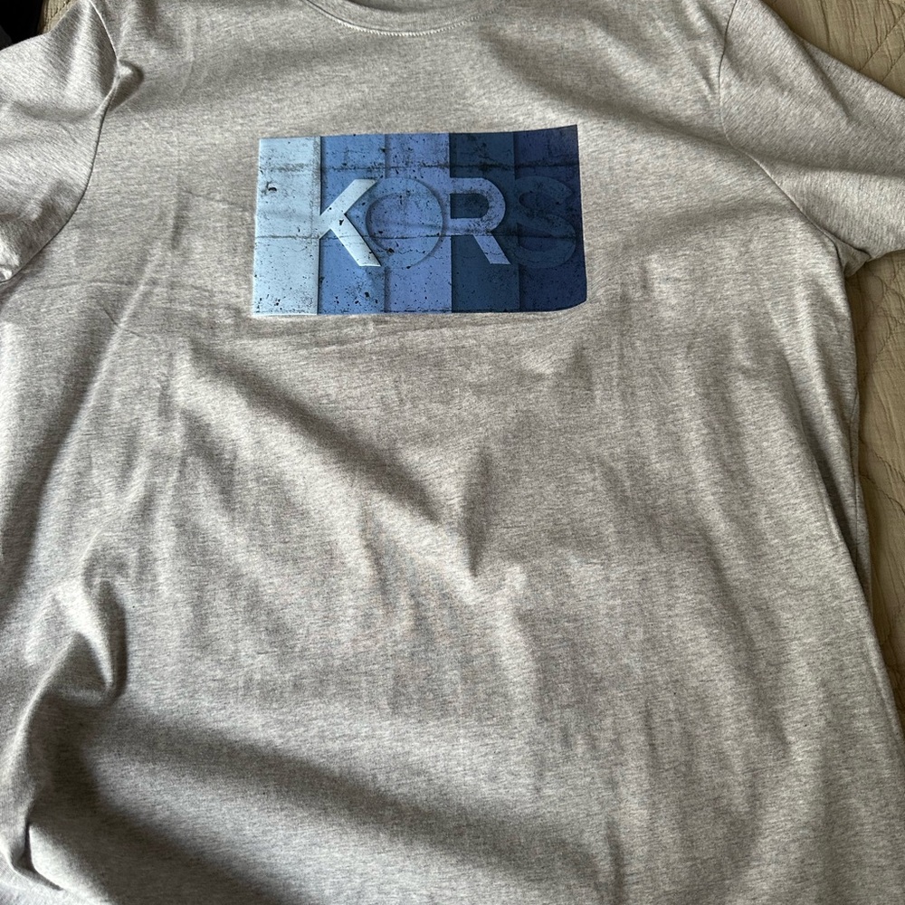 Two Michael Kors t shirts on black and white other gray with blue print.